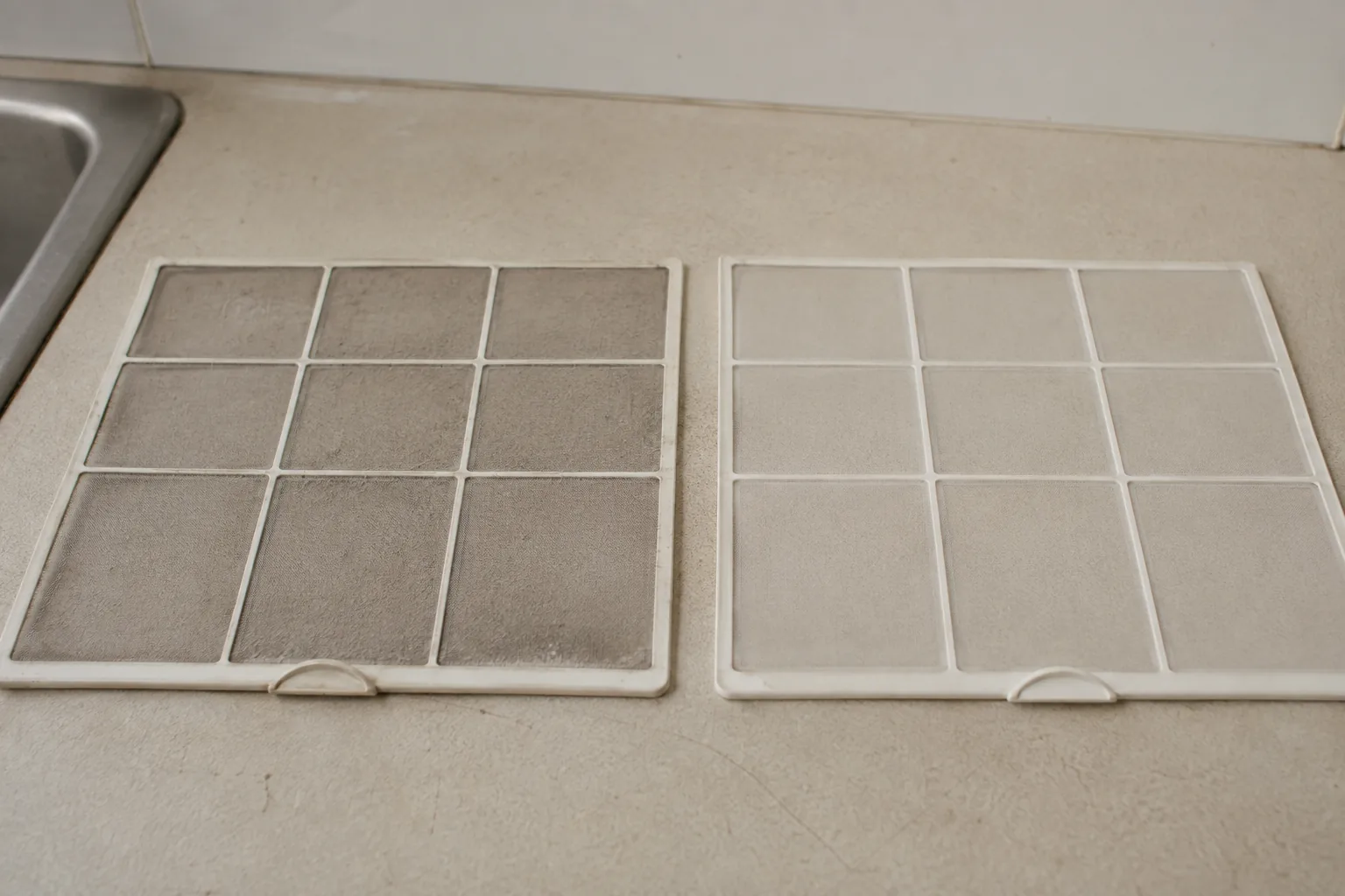 Two split system filters on a countertop side by side, the left one grey and dust-caked, the right one clean and white, showing the difference restricted airflow makes