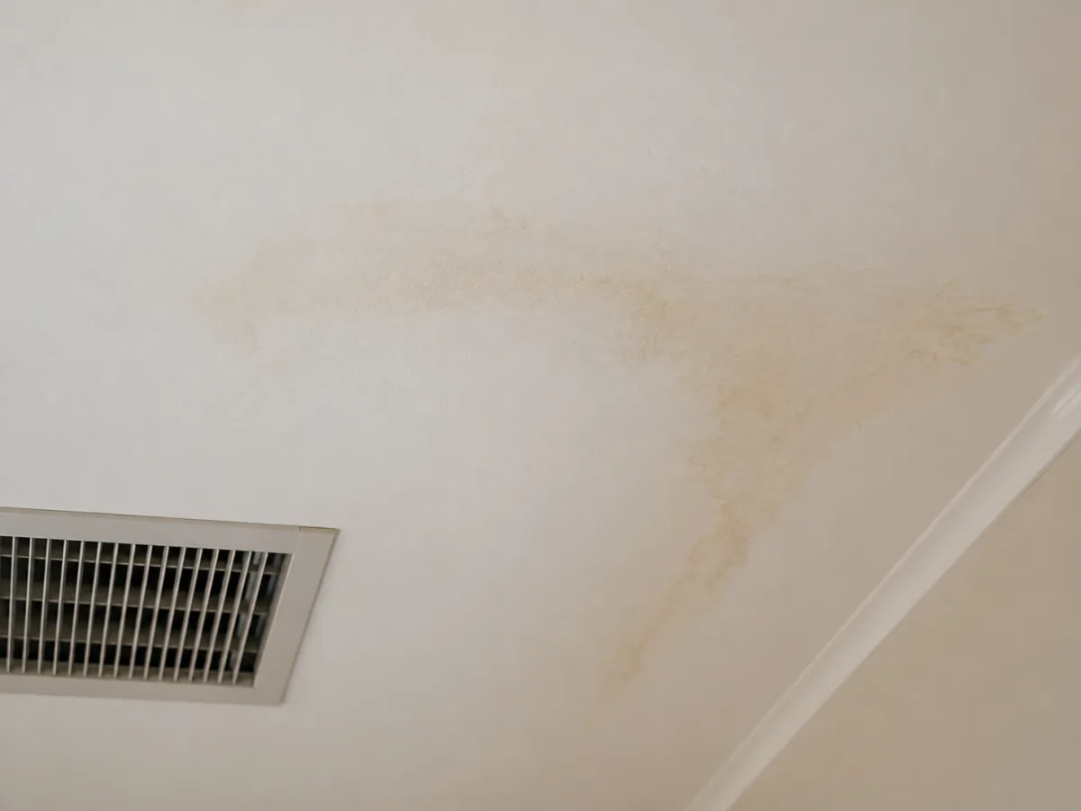 Brown water stain spreading across a white ceiling near a rectangular ducted air conditioning outlet, showing damage caused by an ongoing condensate leak