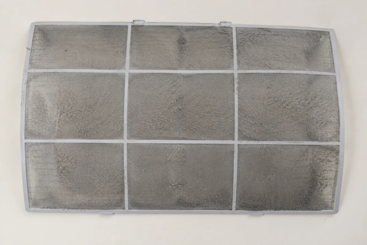 Heavily dust-caked split system air conditioner filter mesh, the single most common contributor to a leak because it starves the coil of airflow