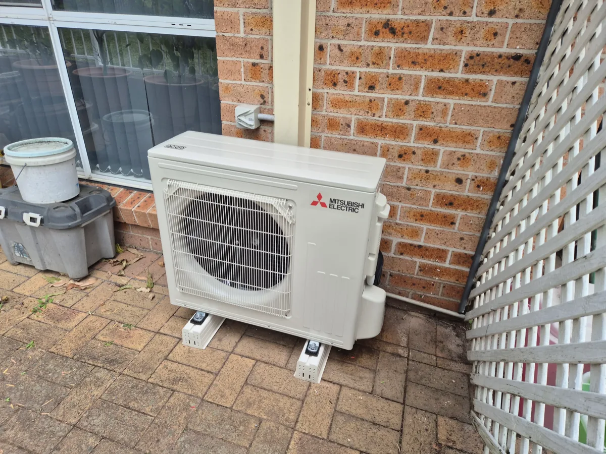 Mitsubishi Electric outdoor condenser mounted on anti-vibration feet on a paved patio against a brick wall