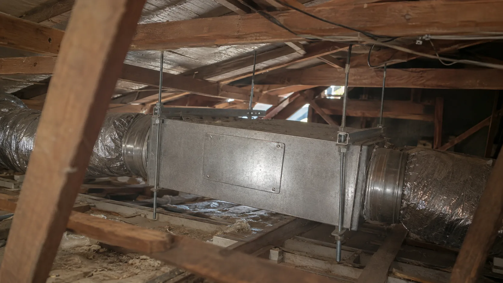 Insulated metal ductwork suspended between wooden roof trusses in an Australian home, showing a new ducted air conditioning installation